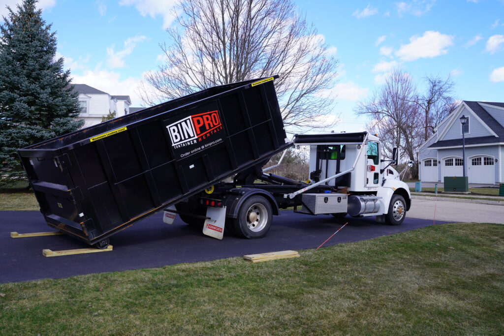 A truck delivering a dumpster with the Bin Pro logo on it.